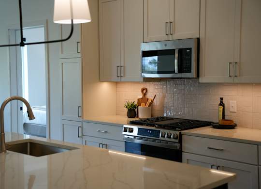 A kitchen with a stove, sink, and cabinets.