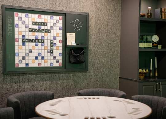 A Scrabble board is on the wall above a table.