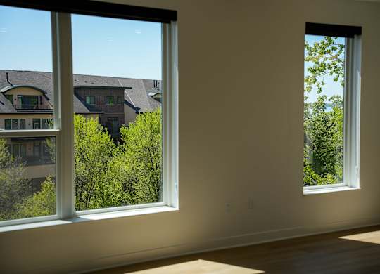 Two windows in a room with a view of houses and trees outside.