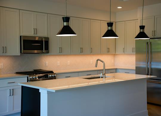 A kitchen with a white counter top and black pendant lights.