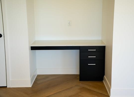 A black desk with two drawers is in a room with white walls.