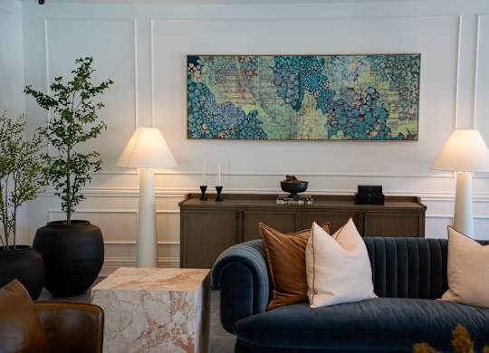 A living room with a black couch and a painting on the wall.