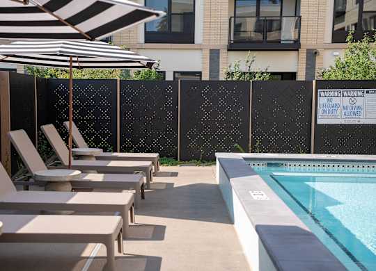 A pool area with sun loungers and a black and white striped umbrella.