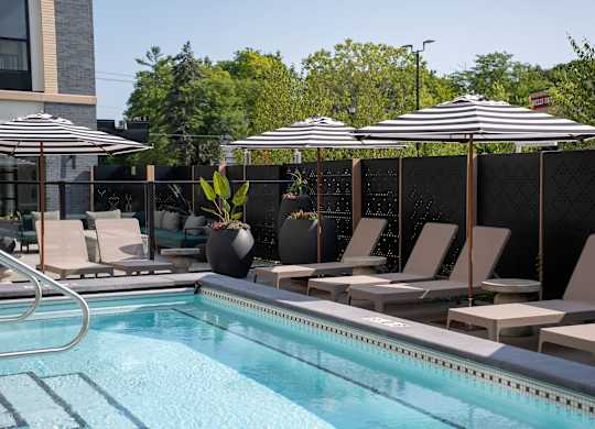 A pool with chairs and umbrellas is surrounded by a black fence.