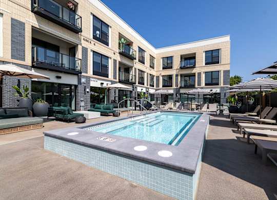 A swimming pool in the middle of a courtyard surrounded by lounge chairs and umbrellas.