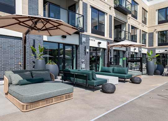 A patio with a green couch and a brown umbrella.