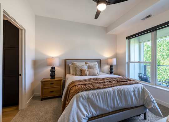 A bedroom with a bed, two lamps, and a ceiling fan.