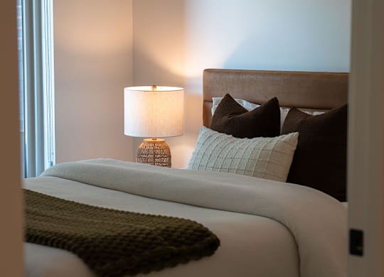 A bed with a white comforter and a brown throw.