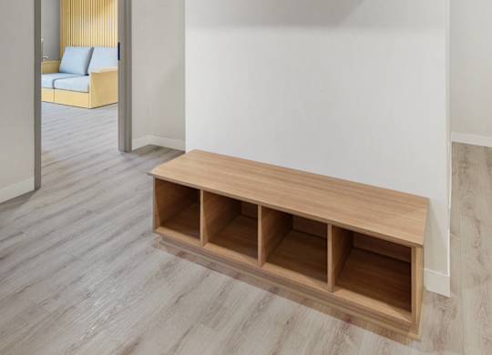 A room with a white wall and a wooden bench with drawers underneath it.