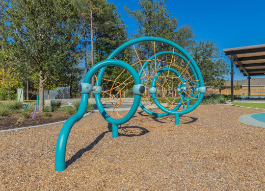 a playground with a blue climbing structure and a basketball court in the background at The Village at Granger Pines, Conroe, 77302