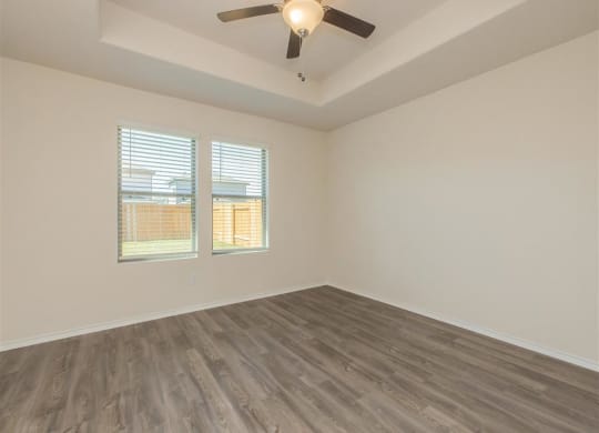 an empty room with a ceiling fan and two windows at The Village at Granger Pines, Conroe, TX 77302