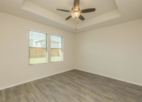 an empty bedroom with a ceiling fan and two windows at The Village at Granger Pines, Texas
