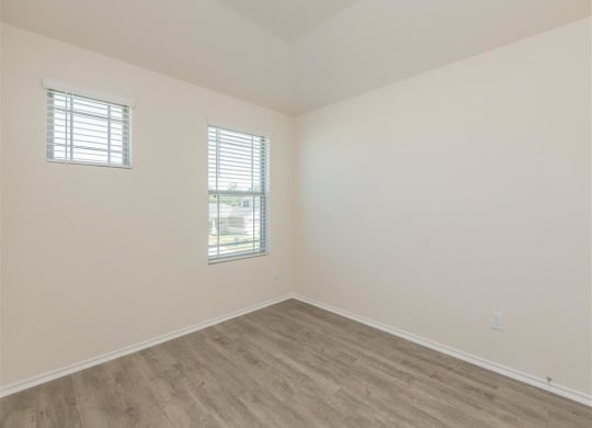 an empty room with two windows and a wooden floor at The Village at Granger Pines, Texas, 77302