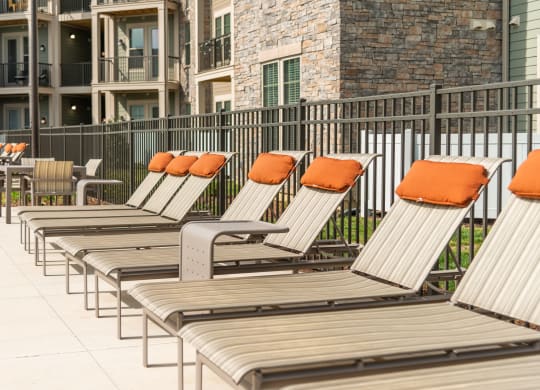a row of lounge chairs with orange pillows in front of an apartment building at The Whitworth, Williamsburg, 23185