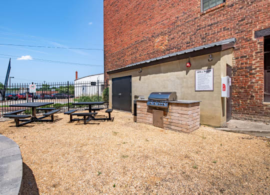 a picnic area outside of a brick building with a grill and picnic table at Mayton Transfer Lofts in Petersburg, VA 