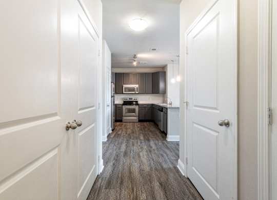 A long hallway with white doors on either side leading to a kitchen.