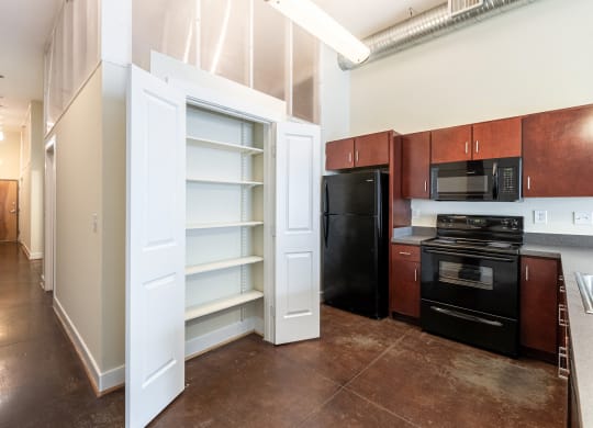 a kitchen with a black refrigerator and black appliances and a white closet with open doors at Mayton Transfer Lofts in Petersburg, Virginia 23803