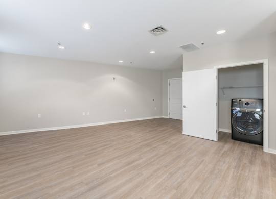 A large empty room with a washing machine in the corner.