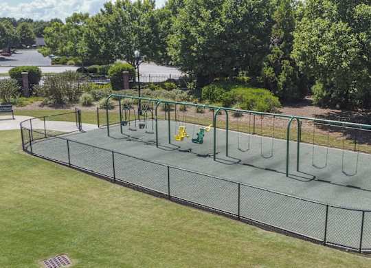 A playground with a green fence and a trampoline.