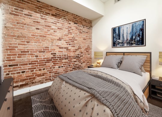 a bedroom with a bed and an exposed brick wall at Mayton Transfer Lofts in Petersburg, VA 23803
