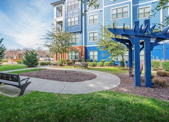 A park area with a bench and a tree in front of a blue building.