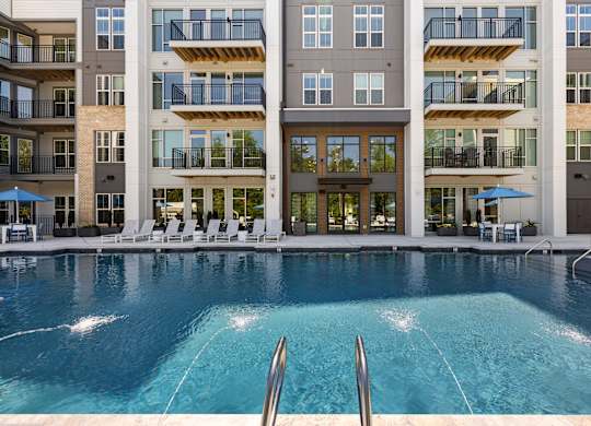 A large swimming pool in front of a multi-story apartment building.