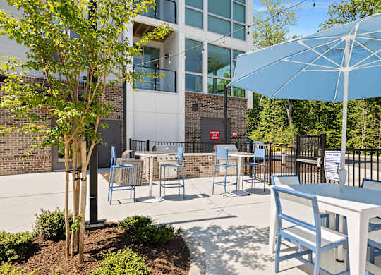 A white table with blue chairs and a white umbrella are on a patio.