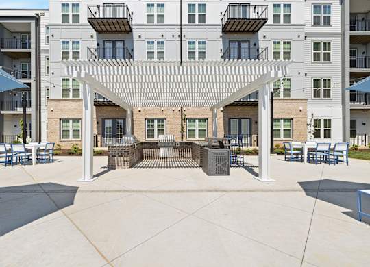 A patio with a white pergola and blue chairs is surrounded by apartment buildings.