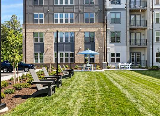 A large grassy area in front of a building with benches and a blue umbrella.