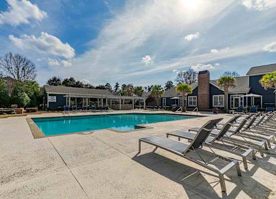 A sunny day at the pool with lounge chairs and a building in the background.