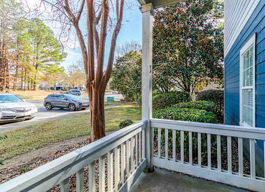 A blue house with a white porch and a tree in front.