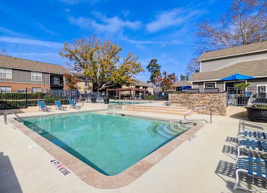 A pool surrounded by chairs and trees.