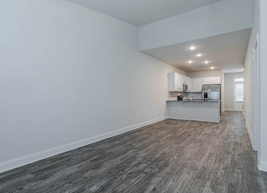 A kitchen with white cabinets and a refrigerator is visible in the background.