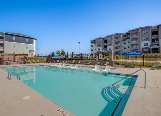 A large swimming pool with lounge chairs and apartment buildings in the background.