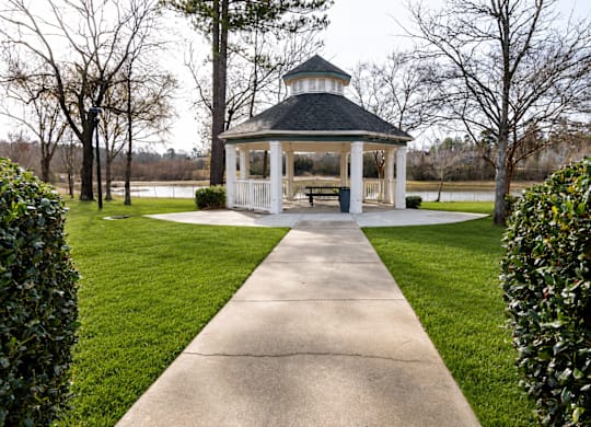 A gazebo is surrounded by green bushes and a concrete walkway.