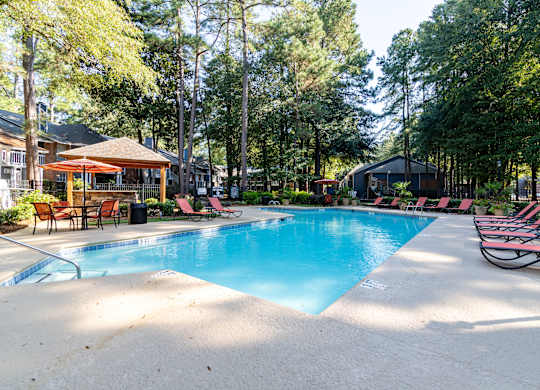 A large swimming pool surrounded by trees and lounge chairs.