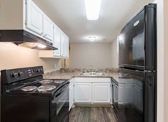 A black stove top oven with four burners and a black refrigerator in a kitchen.