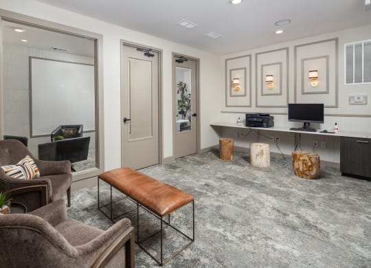 a living room with gray carpeting and a gray desk with a computer and a brown leather at The Flats at Southlawn Apartments, Lawrenceville