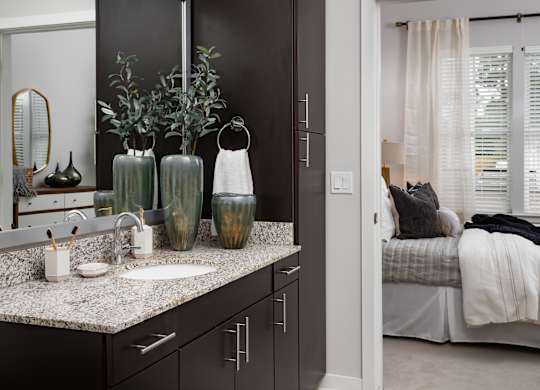 A bathroom with a sink, mirror, and vases on the counter.