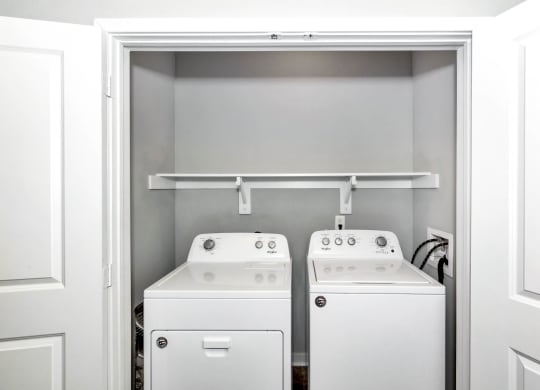 a white laundry room with two washes and a dryer at Farmhaus Apartments, Alabama