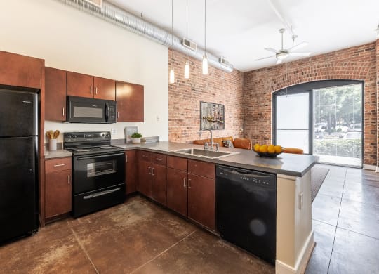 a kitchen with black appliances and wooden cabinets and a brick wall at Mayton Transfer Lofts in VA 23803