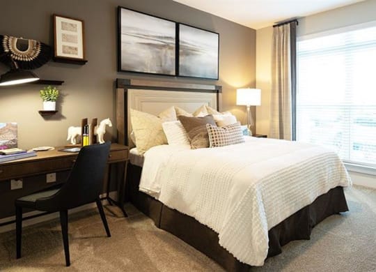a bedroom with a bed and a desk and a window at The Flats at Southlawn Apartments, Lawrenceville, GA 30046