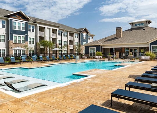 a swimming pool with lounge chairs in front of an apartment building at Promenade at Newnan Crossing, Newnan, GA 30265