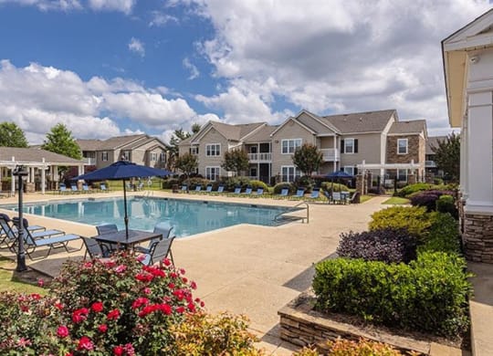 a swimming pool with chairs and umbrellas in front of houses at Bedford Parke Apartments, Warner Robins, GA