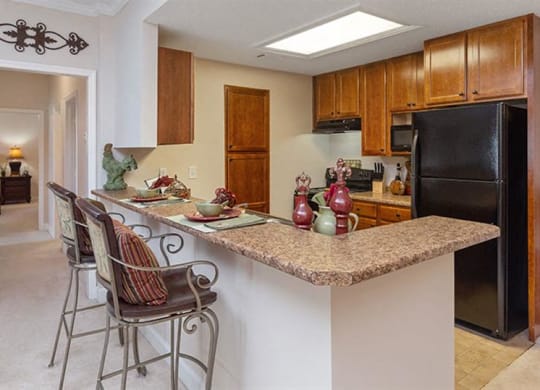 a kitchen with a bar with three chairs at Bedford Parke Apartments, Warner Robins, GA