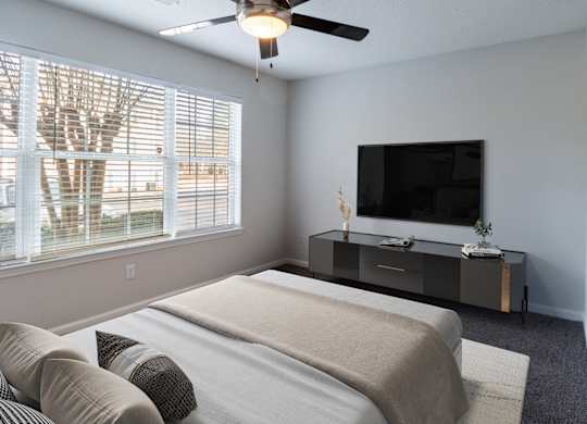 A bedroom with a bed, a television, and a window with blinds.