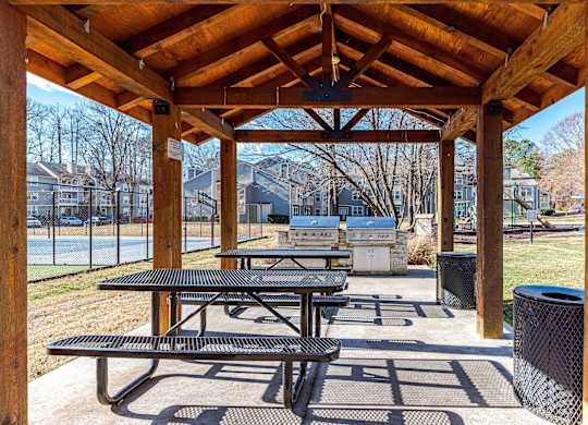 A wooden pavilion with picnic tables and a basketball court in the background.