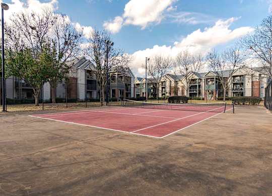 A tennis court is surrounded by apartment buildings.