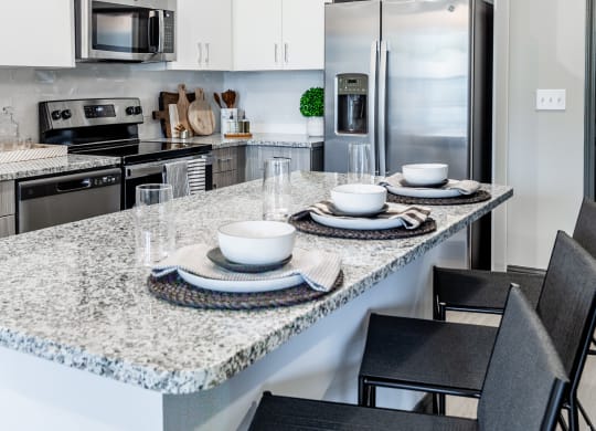 an open kitchen with a marble counter top and a large island with plates and bowls at The Louis Apartment Flats, Louisville, 40241