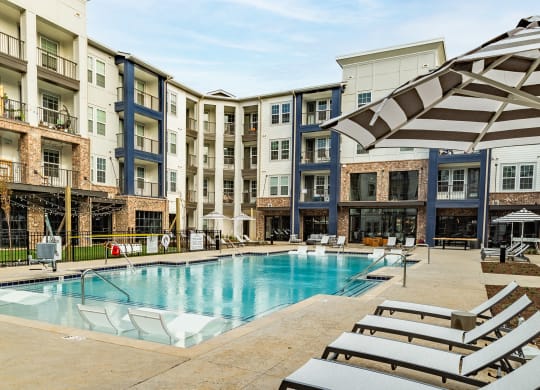 a swimming pool with beach chairs in front of an apartment building at The Louis Apartment Flats, Kentucky, 40241